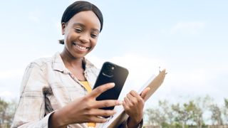 Mulher segurando iPhone e prancheta em um campo